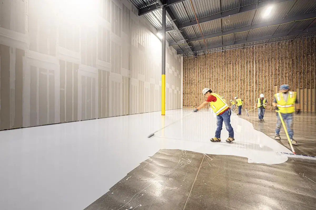 a crew in high-visibility vests coating a warehouse floor